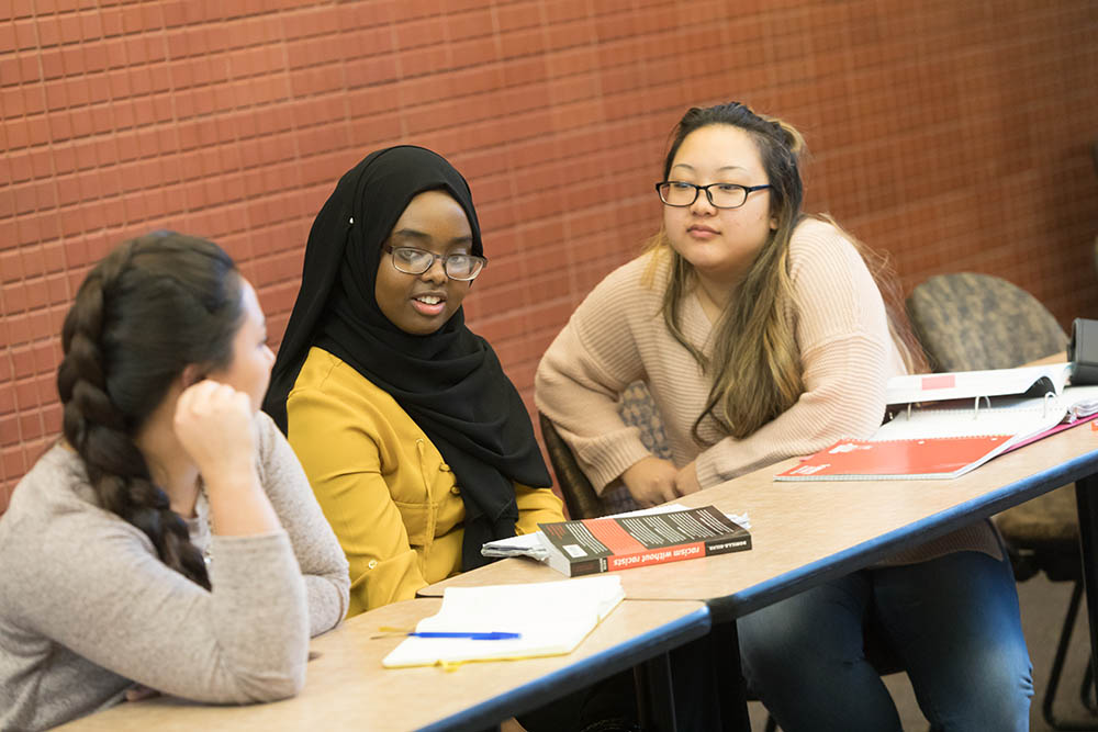 Three students studying together, with books and notes on the table in front of them.