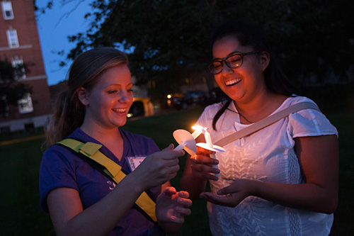 Two students lighting each other vigil candle at night