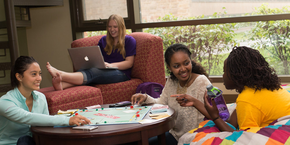 Four students socializing and playing board games in their dorm common area.