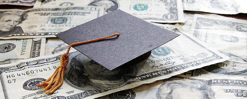 Staged photo of graduation cap placed on top of a pile of cash