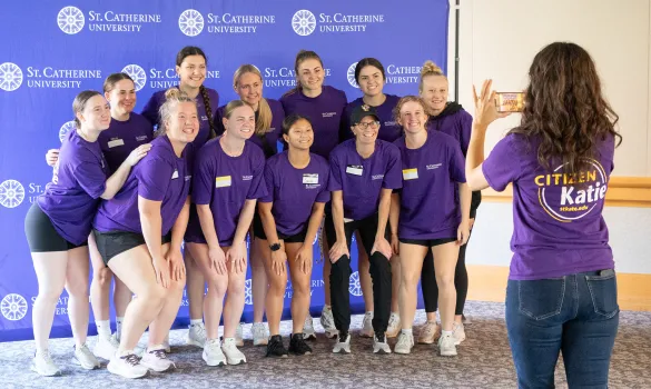 A group of students wearing purple T-shirts pose for a photo taken by someone holding a phone